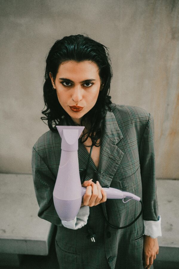 Stylish adult holding a purple hairdryer indoors, showcasing modern fashion.